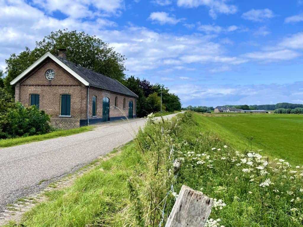 Kleurrijk boerderijtje met groene ramen en een gravelpad in een landelijke omgeving.
