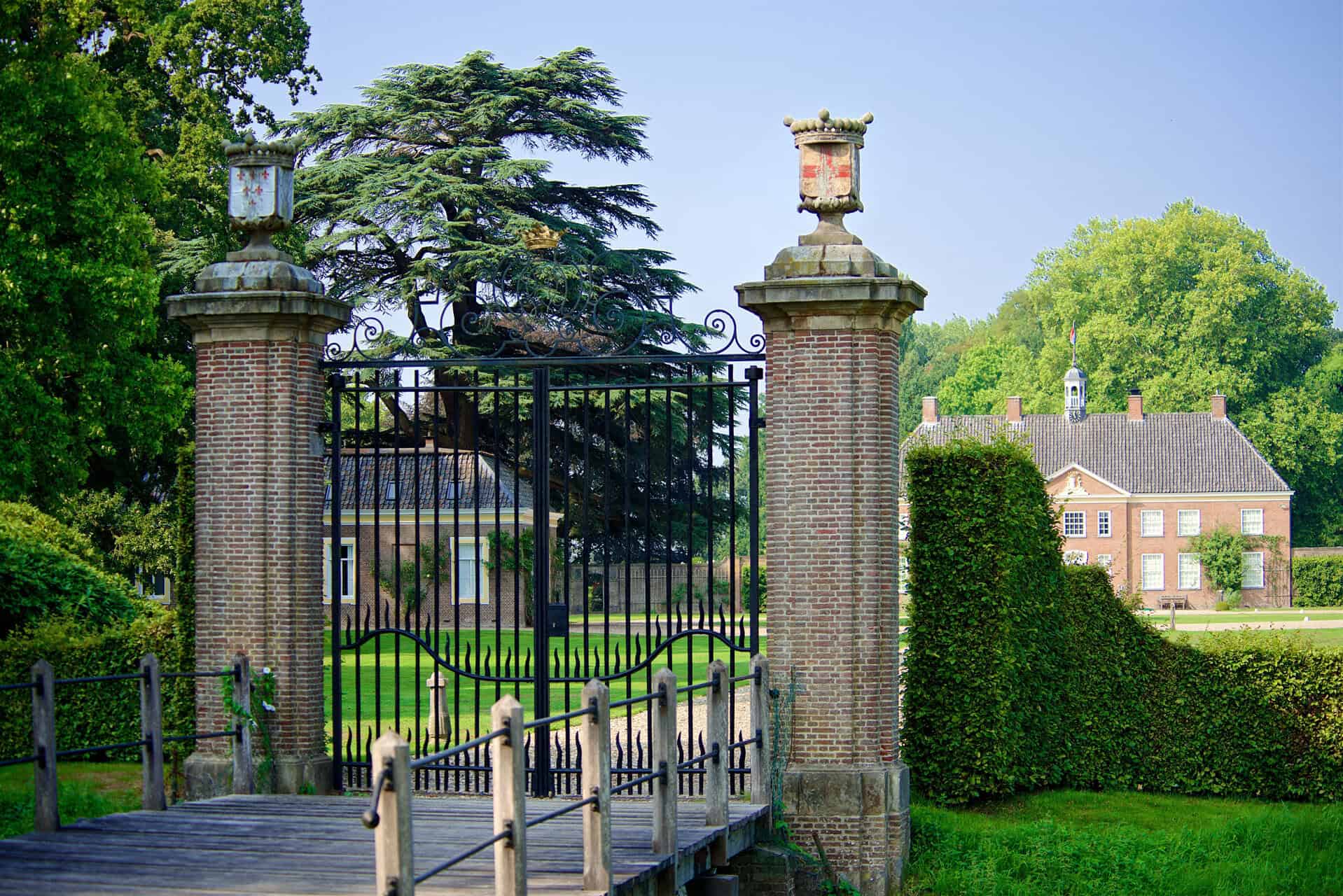 Oude ijzeren poort met stenen zuilen en groene tuin erachter.
