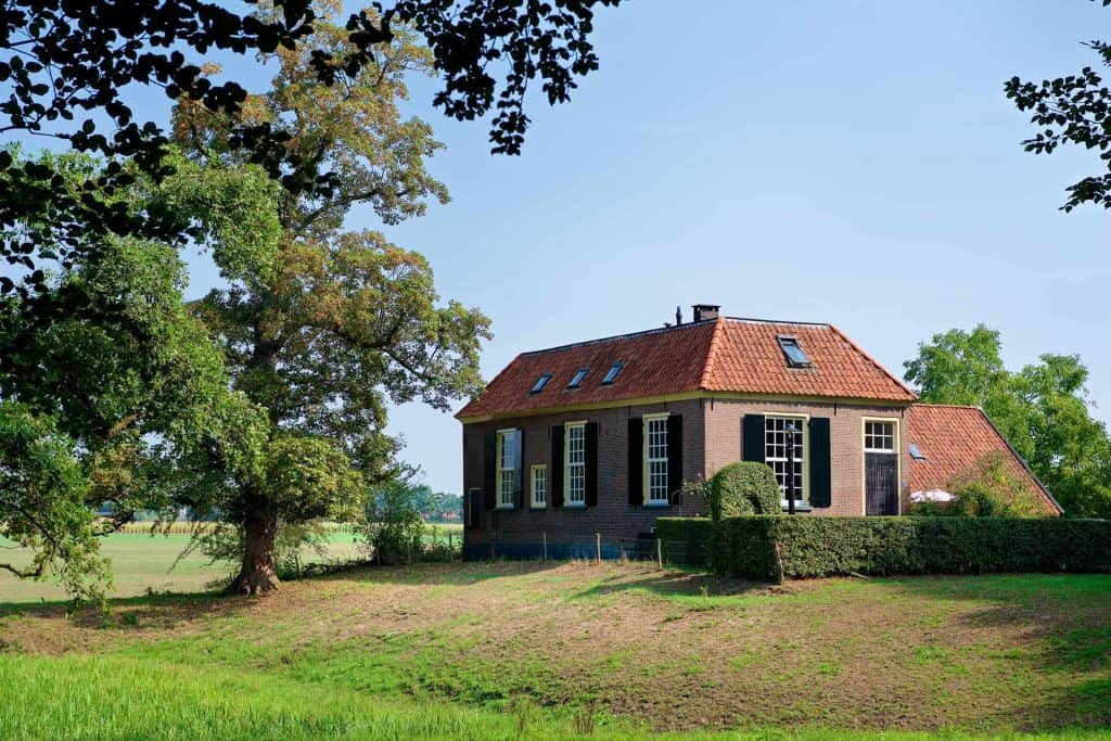 Landhuis met rood dak en grote ramen in groene omgeving.