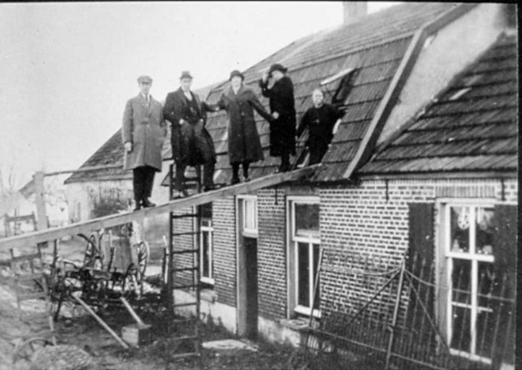 Mensen op het dak van een huis op 't Gelders Eiland, oude zwart-wit foto.