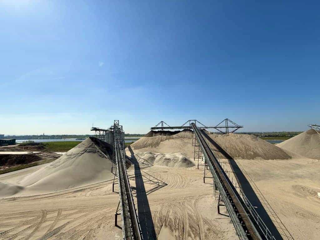 Zandwinning op 't Gelders Eiland met grote zandhopen en industriële machines.