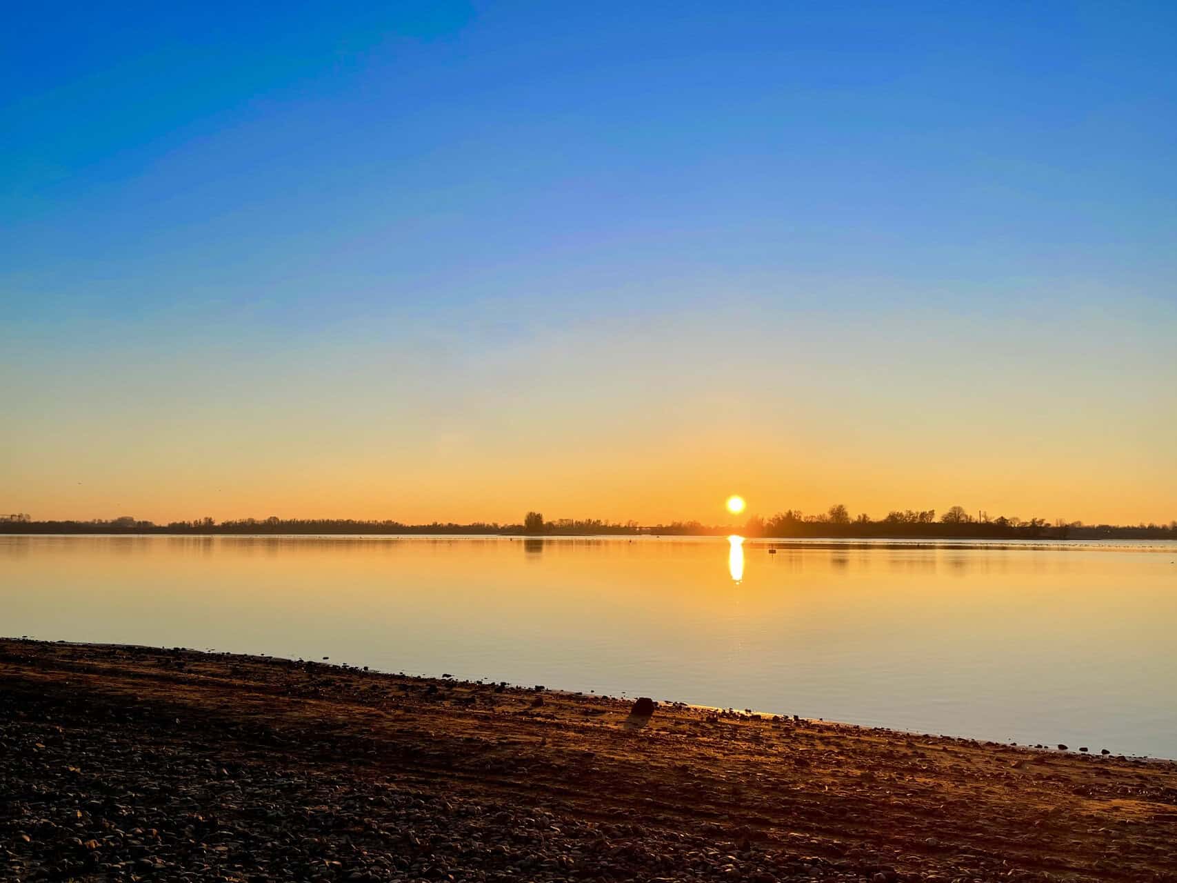 Zonsondergang boven water op 't Gelders Eiland met rustige rivier en heldere hemel.