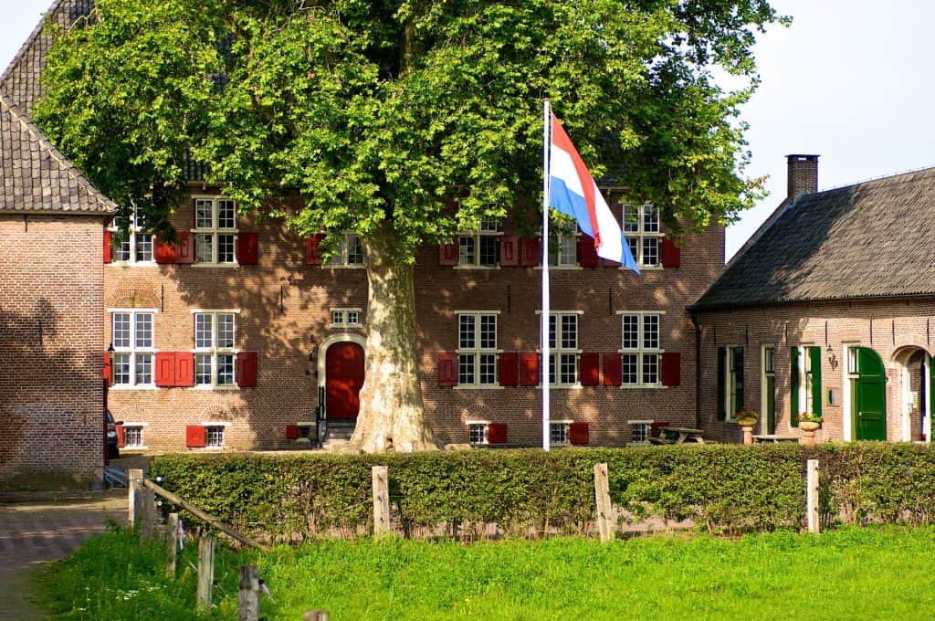 Gezellig huis op 't Gelders Eiland met grote boom en Nederlandse vlag, omgeven door groen en histori.