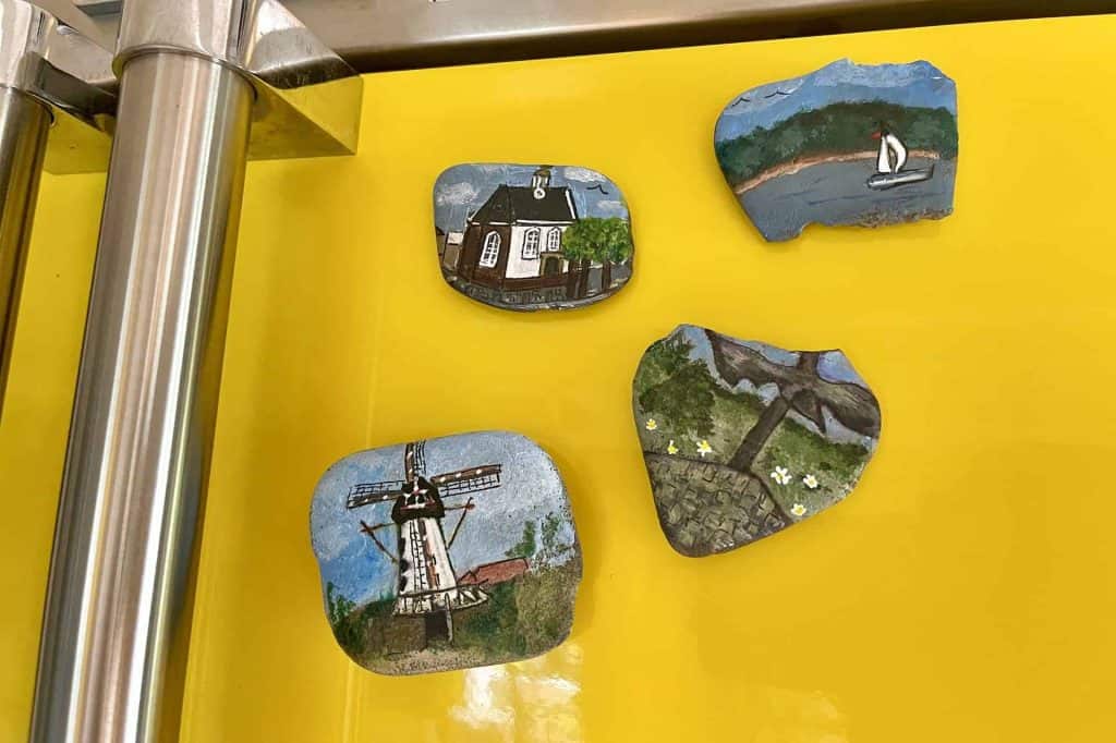Handgeschilderde koelkastmagneten met landschap en molen op geel muur.