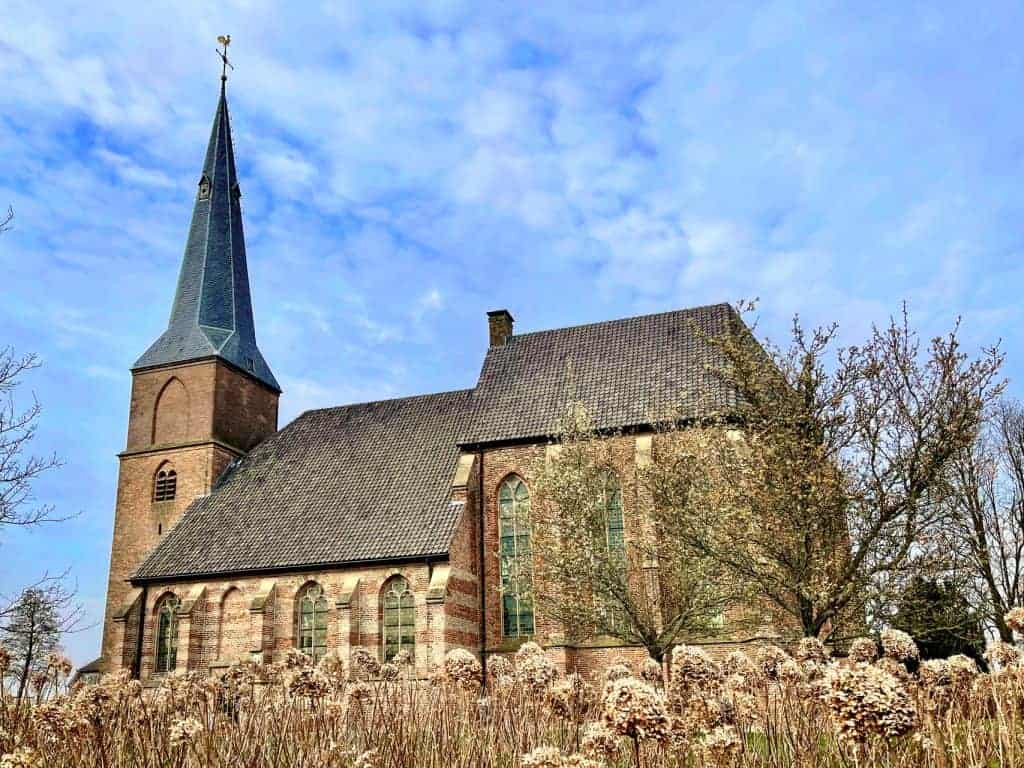 Kerk op 't Gelders Eiland met een hoge toren en historische architectuur, omgeven door bomen en een.
