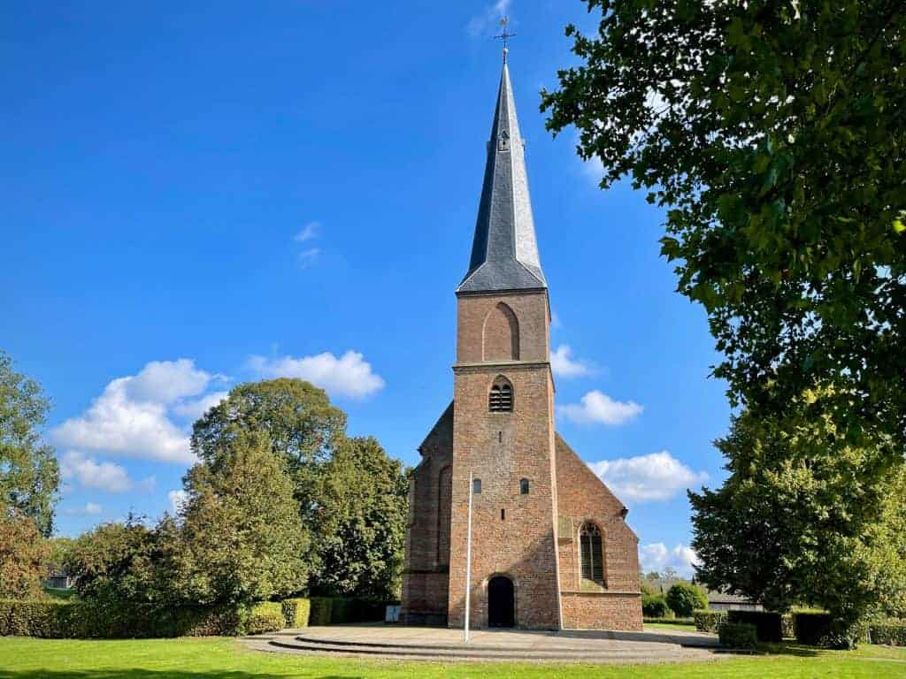Kerk op 't Gelders Eiland met een hoge spits onder een blauwe hemel.