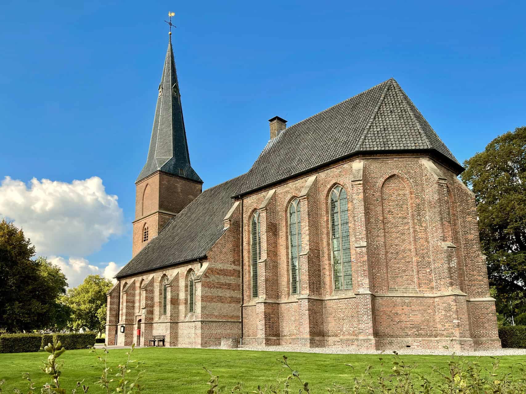 Kerk op 't Gelders Eiland met steeple en rode bakstenen, omgeven door groen gras en bomen.