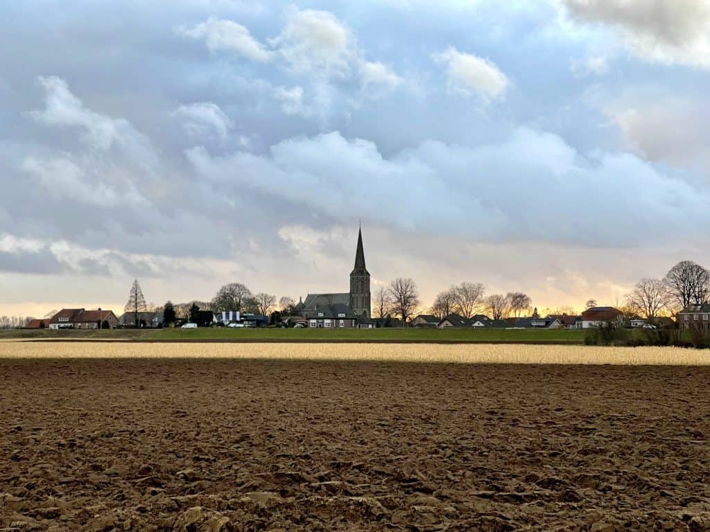 Uitzicht op het landschap van 't Gelders Eiland met kerk en velden onder een bewolkte hemel.