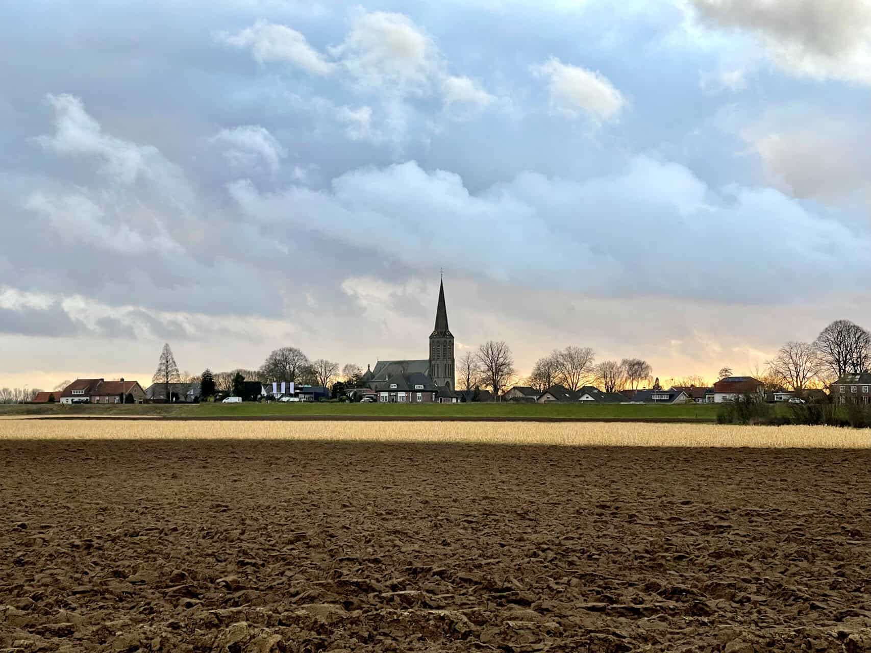 Uitzicht op het landschap van 't Gelders Eiland met kerk en velden onder een bewolkte hemel.