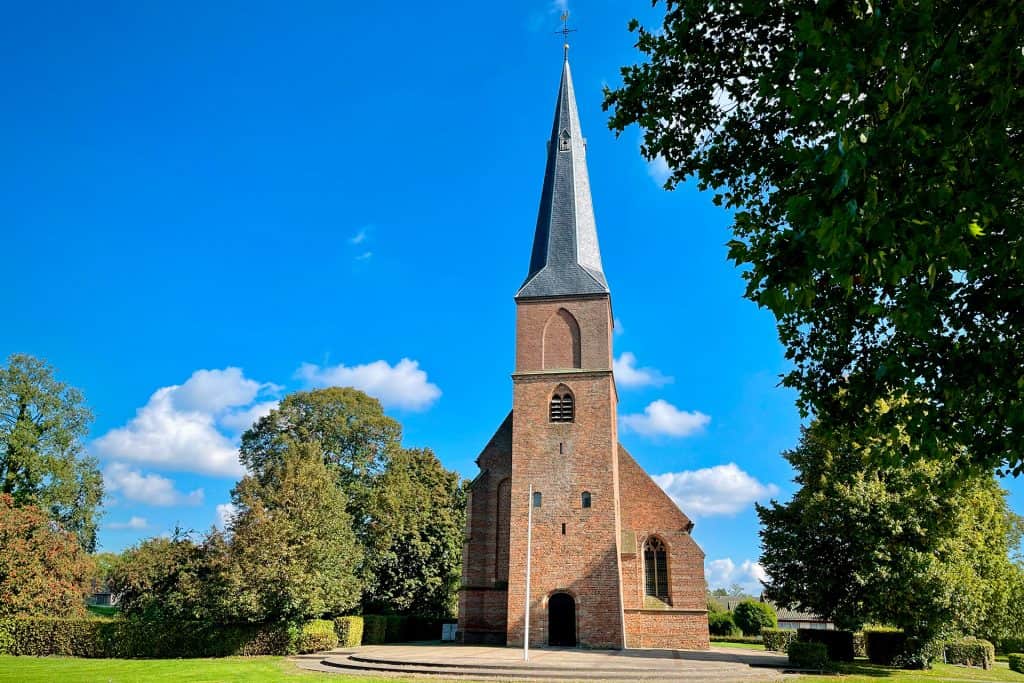 Historische kerk op 't Gelders Eiland met hoge toren en groene omgeving.