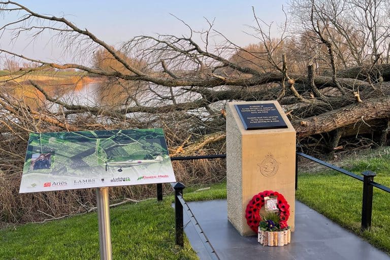 Herdenkingsmonument op 't Gelders Eiland met krans en informatiebord, gelegen aan de rivier met bome.