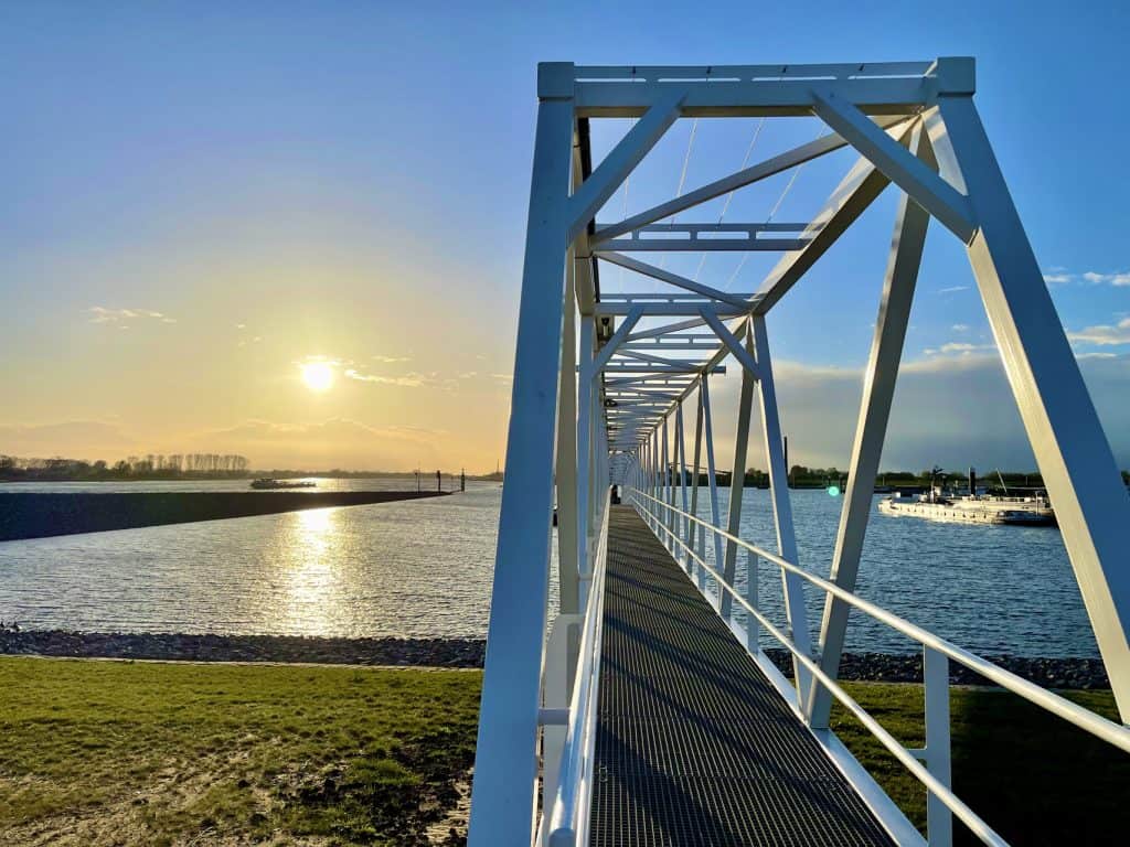 Voetgangersbrug op 't Gelders Eiland bij zonsondergang, water en blauwe lucht.