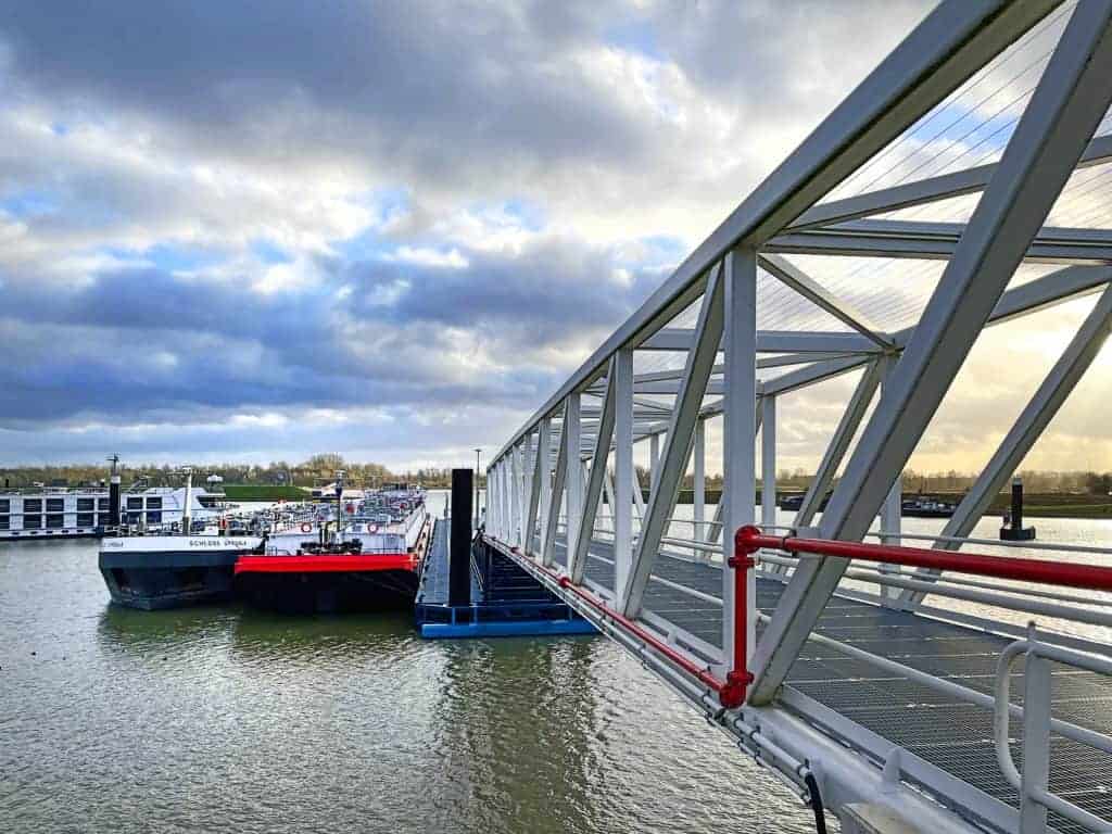 Veerboot en brug op 't Gelders Eiland bij zonsondergang, water en wolken in de achtergrond.