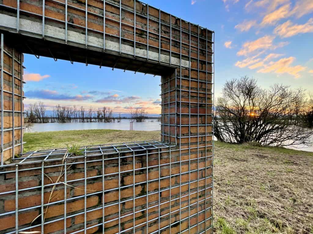 Uitzicht op de rivier door een open raam in een muur van bakstenen en gaas.