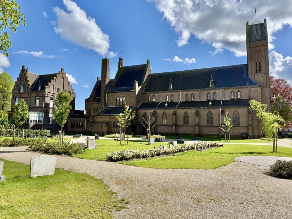 Kerk op 't Gelders Eiland met groene tuin en wandelpaden onder een blauwe hemel.