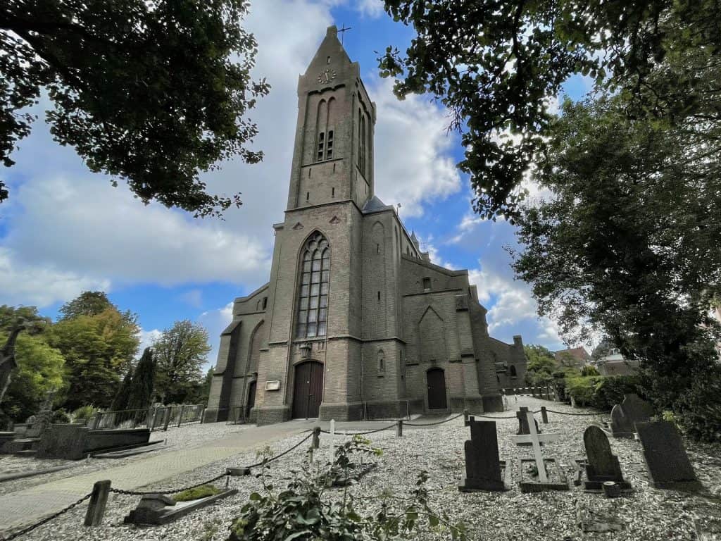 Kerk op 't Gelders Eiland met omliggende begraafplaats, omgeven door bomen en grafstenen, onder een.