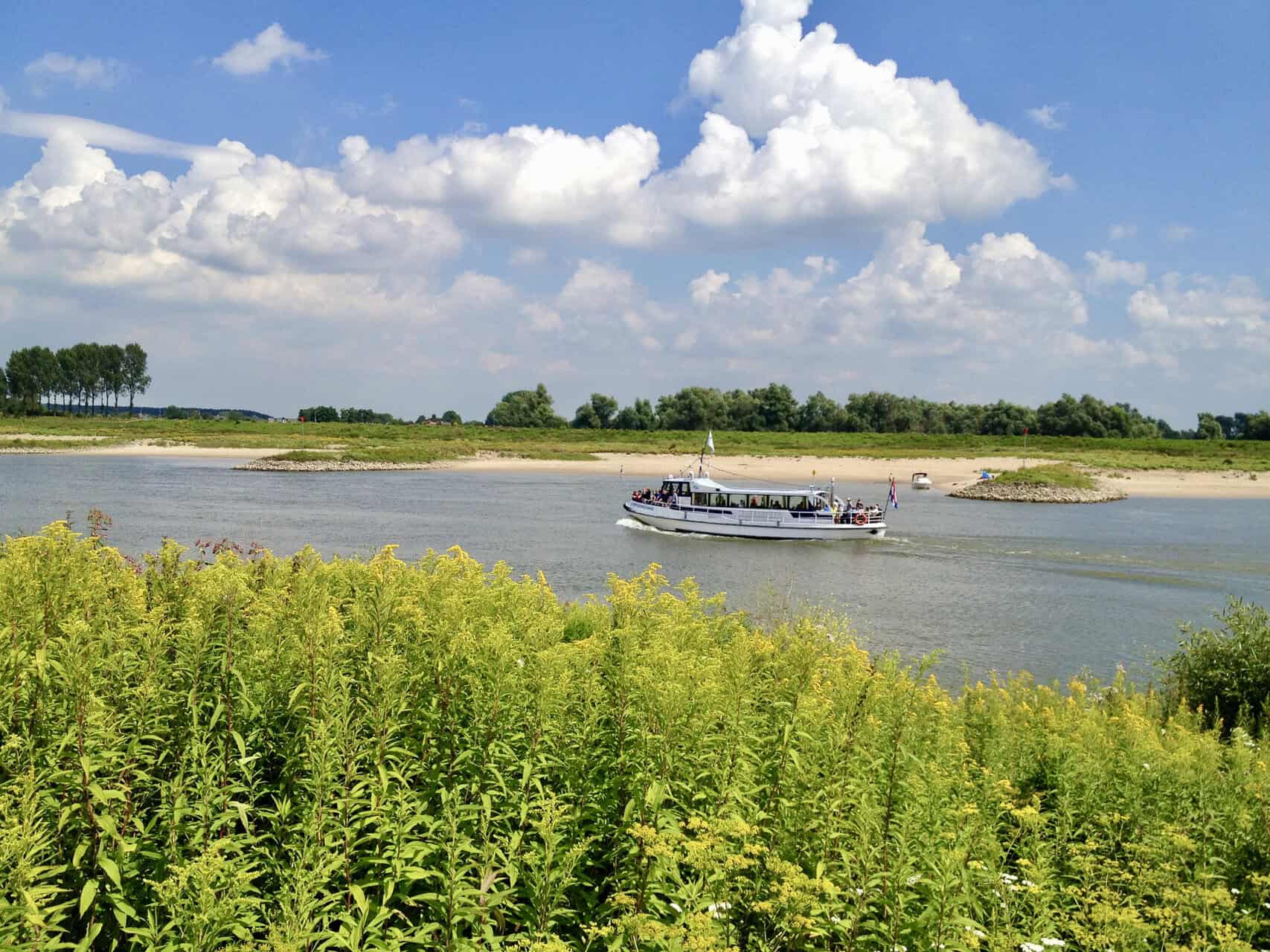 Boot op de rivier met groene oevers en blauwe lucht.