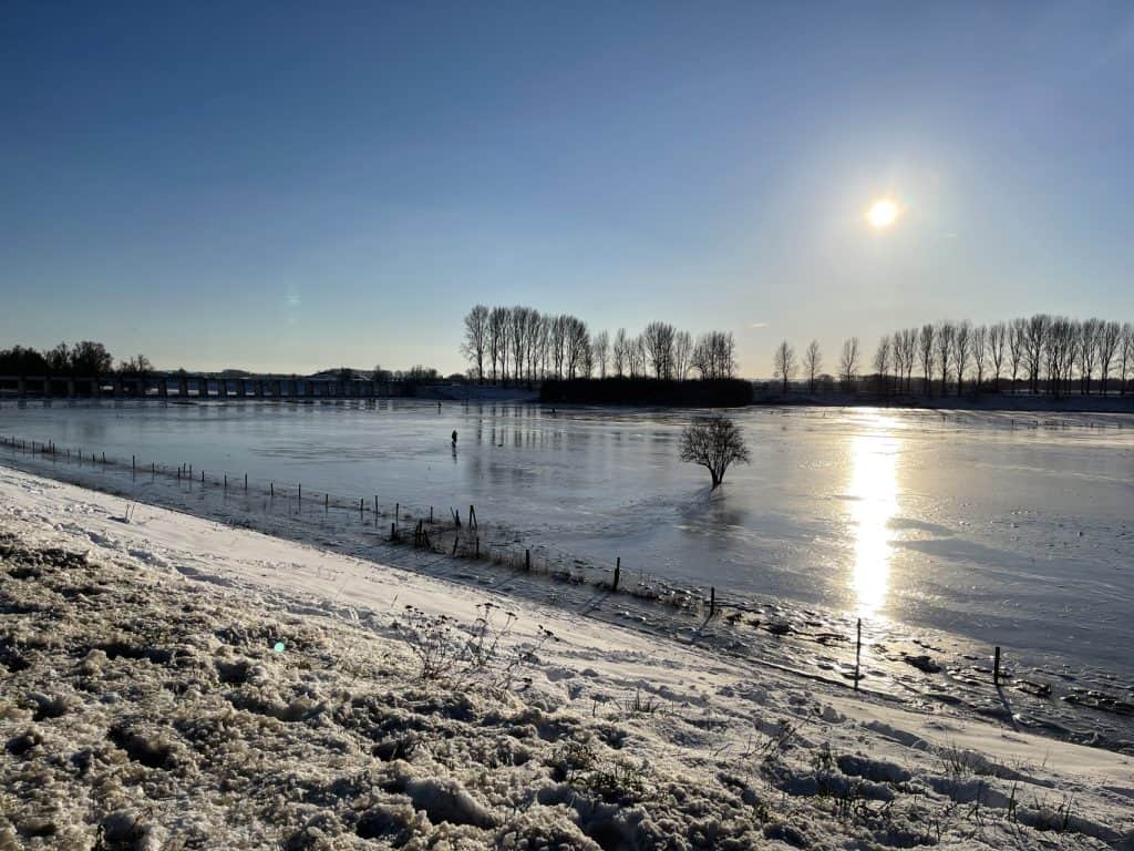 Bevroren rivier en winterlandschap op 't Gelders Eiland onder een heldere blauwe hemel.