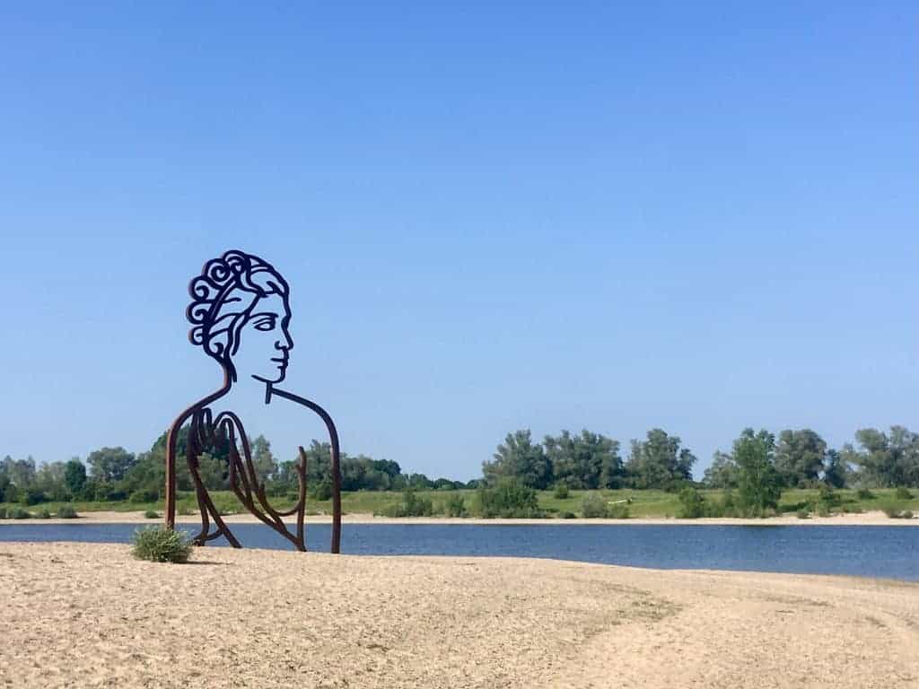 Kunstwerk van een vrouw in een landschap met rivier en groene bomen op 't Gelders Eiland.