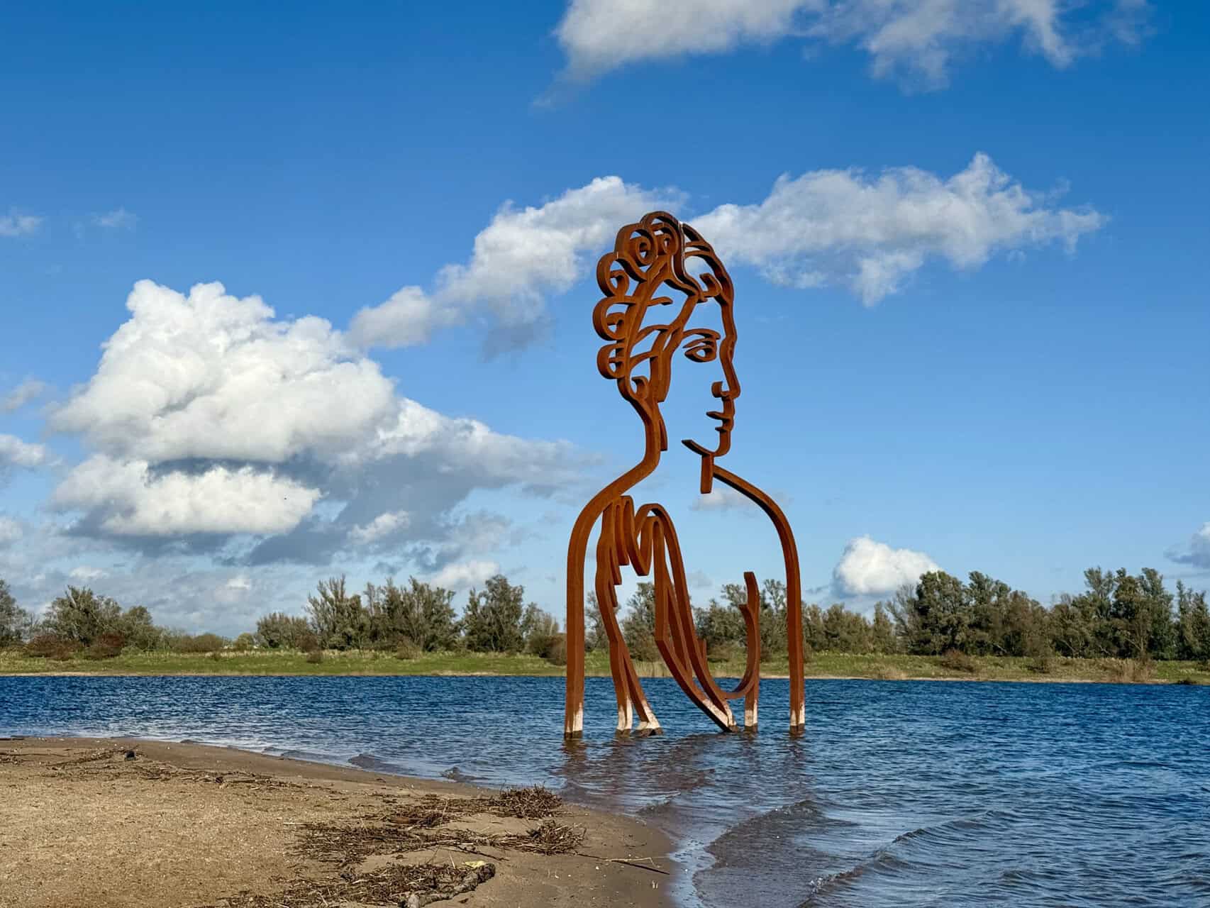 Kunstwerk van een grote metalen vrouwengestalte in het water op 't Gelders Eiland, met een heldere b.