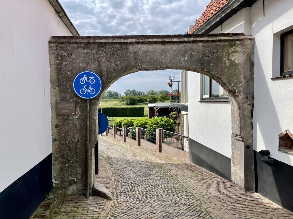 Oude doorgang tussen witte huizen op 't Gelders Eiland met fietsroutebord.