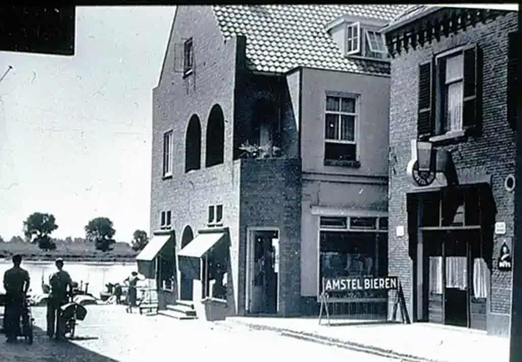 Oude foto van gebouwen en straat op 't Gelders Eiland met winkel en mensen.
