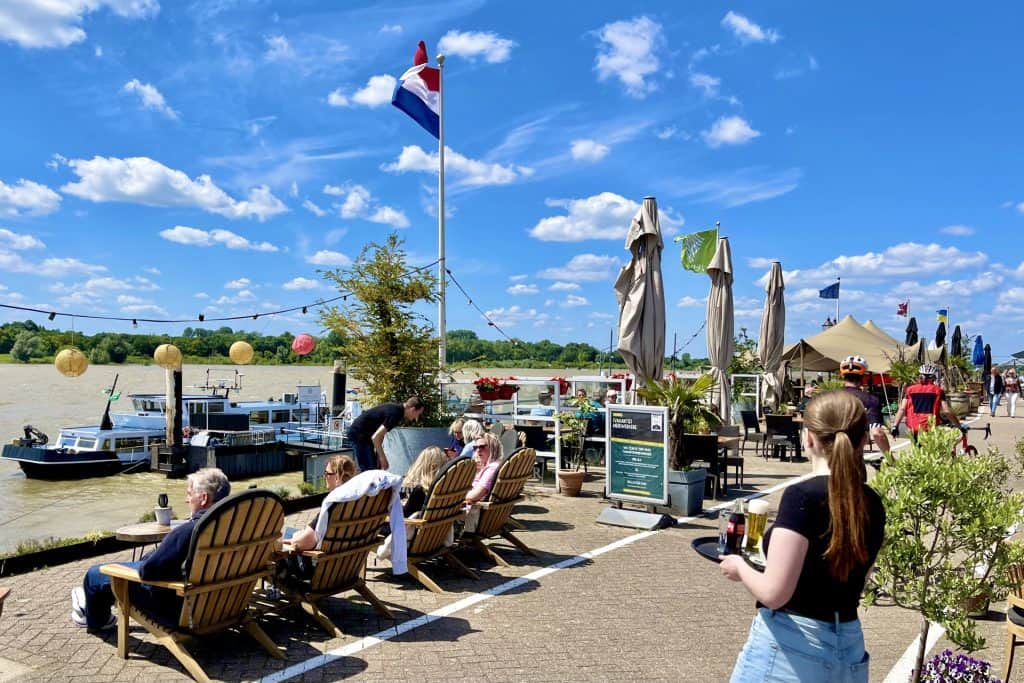Terras met mensen aan de rivier op 't Gelders Eiland, zonnige dag met blauwe lucht.