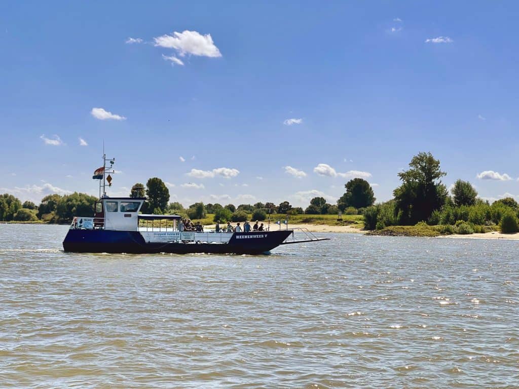 Vaarboot op de rivier met groene oevers en blauwe lucht.