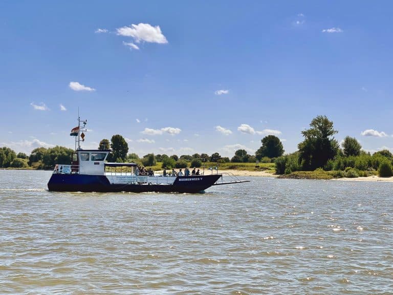 Vaarboot op de rivier met groene oevers en blauwe lucht.