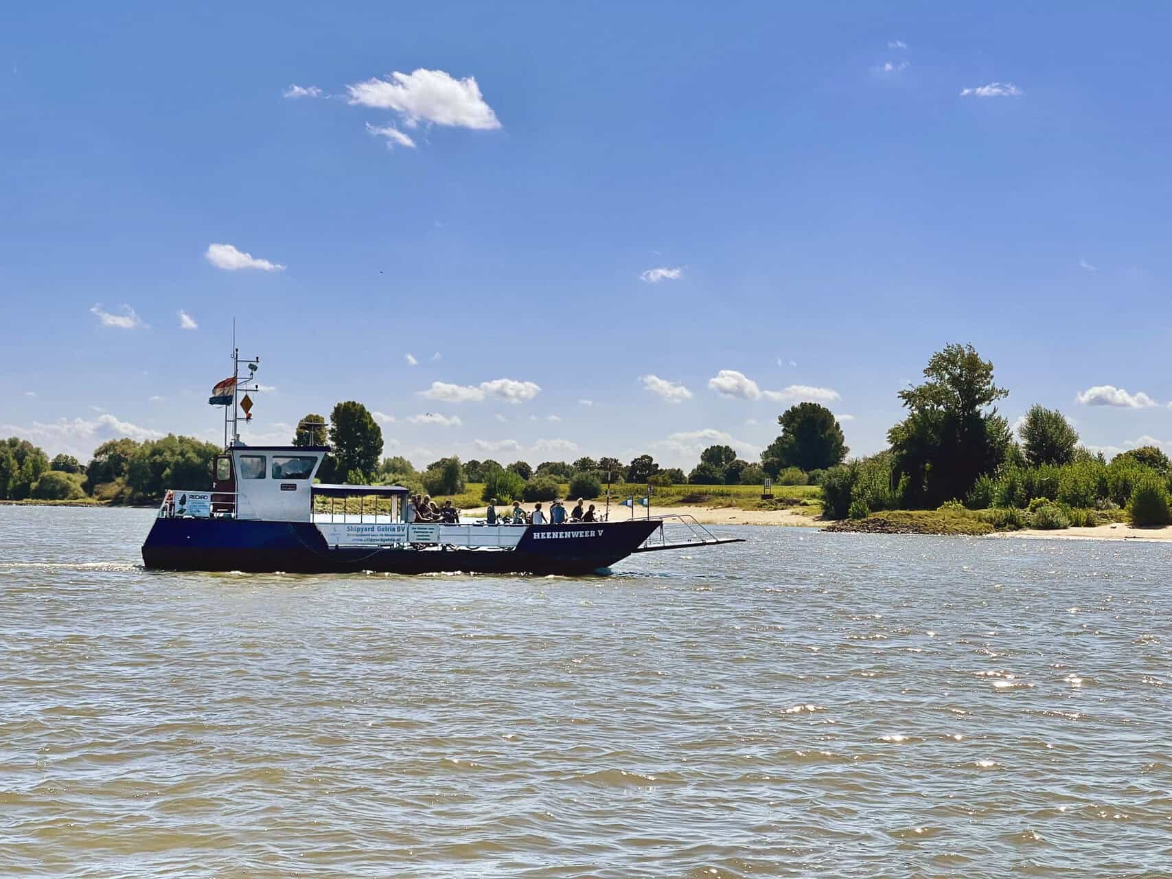 Vaarboot op de rivier met groene oevers en blauwe lucht.