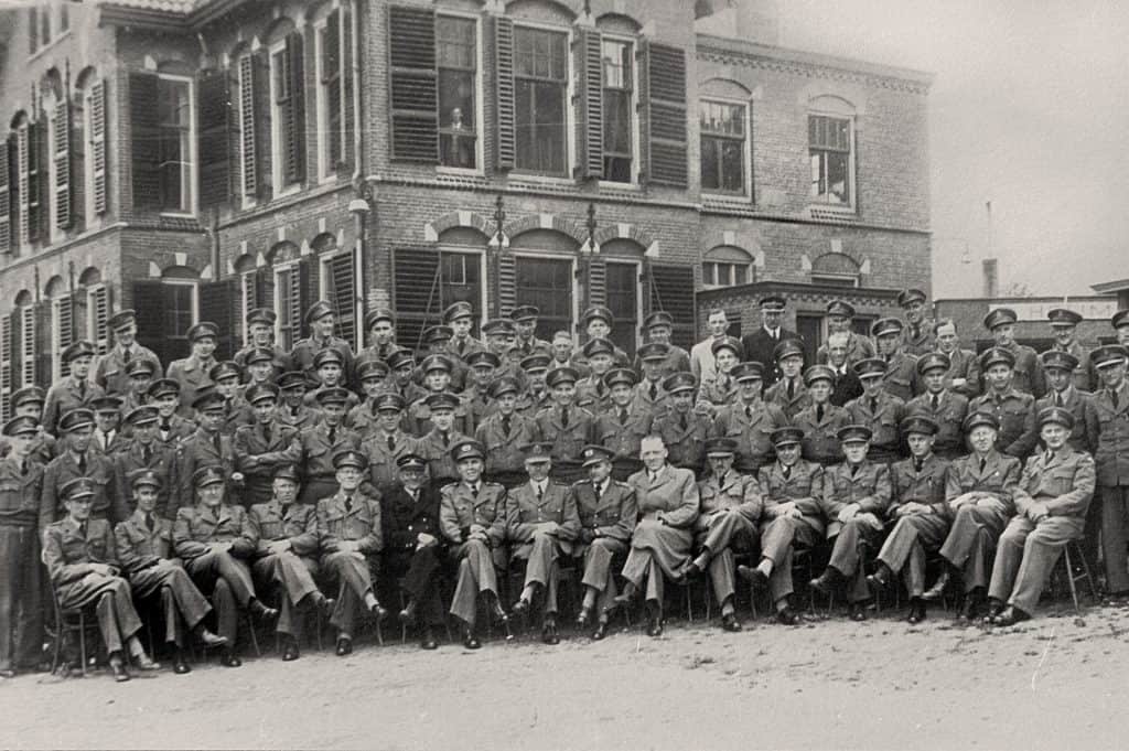 Groep mensen poseert voor een oud gebouw, zwart-wil foto.