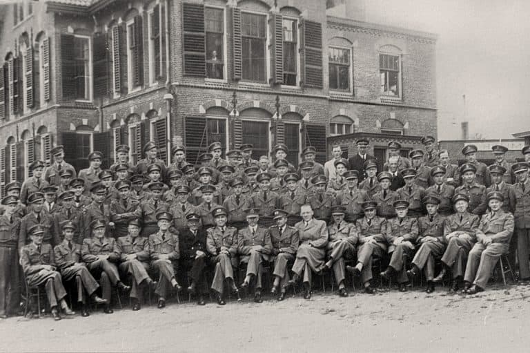Groep mensen poseert voor een oud gebouw, zwart-wil foto.