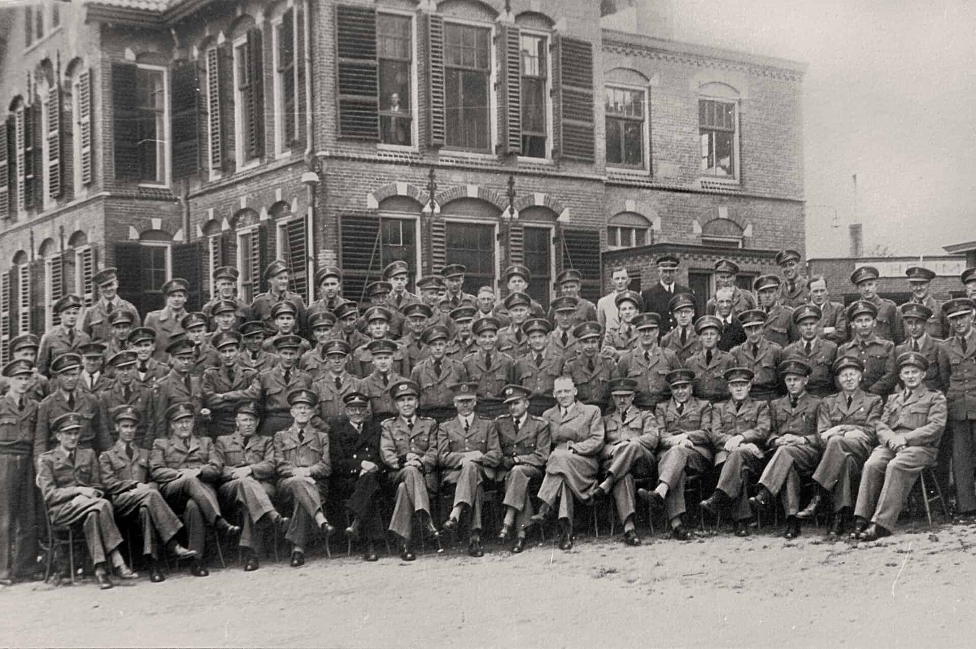 Groep mensen poseert voor een oud gebouw, zwart-wil foto.