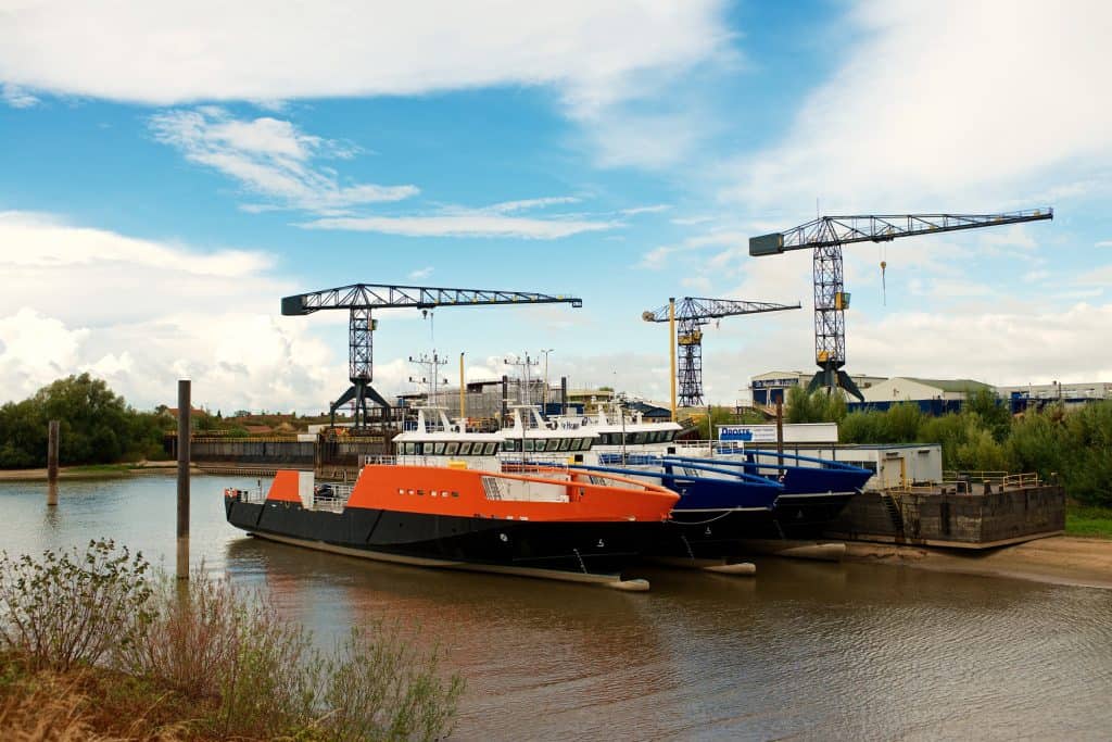 Drie schepen aan de kade met bouwkranen op de achtergrond.