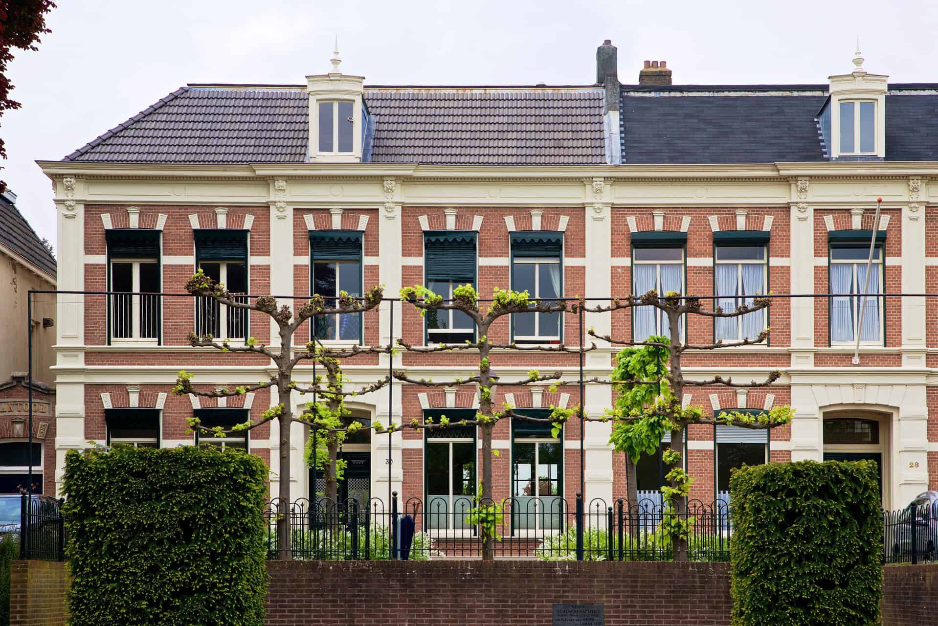 Gezicht op een oud, mooi huis met een tuin en gesnoeide bomen.