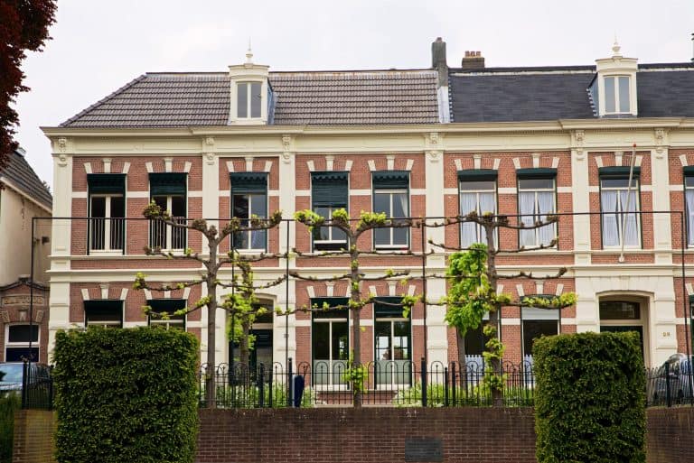Gezicht op een oud, mooi gebouw met groene bomen en een hek.