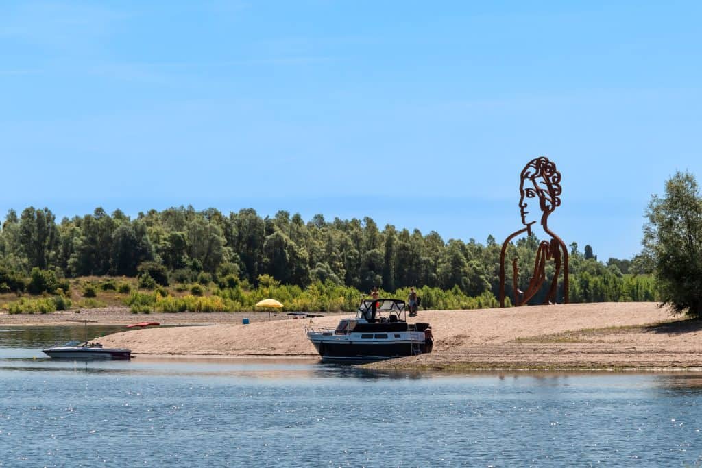Groot beeld van een vrouw op 't Gelders Eiland met rivier en boten.