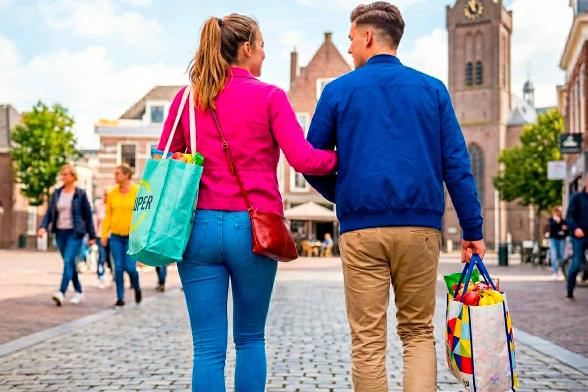 Gezinnen wandelen op 't Gelders Eiland, met winkels en historische gebouwen op de achtergrond.