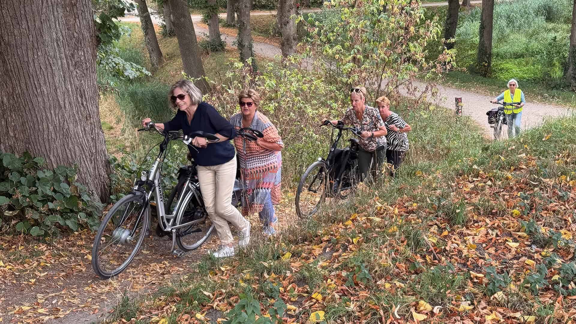Vrouw met fiets en groep wandelaars in bosrijke omgeving.