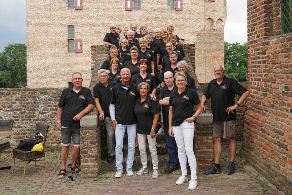 Gezelschap van 20 mensen in zwart T-shirt voor een kasteelmuur.