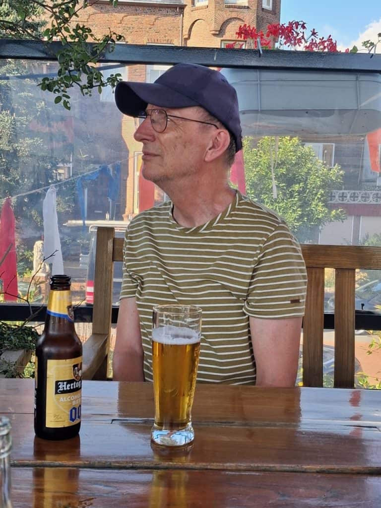 Man met pet, glas bier, en zonnebril op terras in Gelderland.