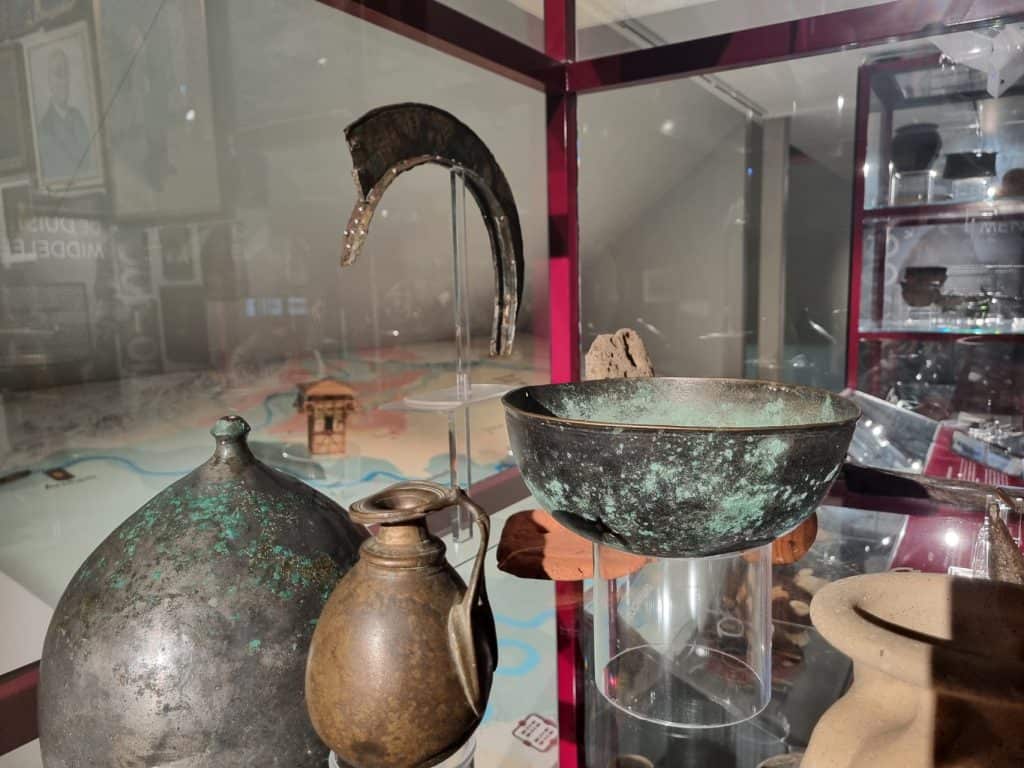 Oude bronzen en aardewerken artefacten in museumdisplay.
