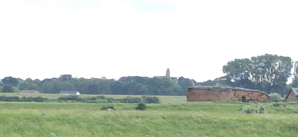 Uitzicht op het landschap van 't Gelders Eiland met groene velden en oude gebouwen.