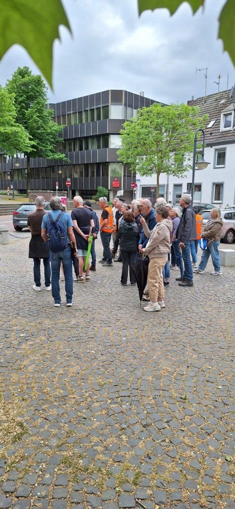 Groep mensen wacht op een gids in een stad met moderne en traditionele gebouwen.