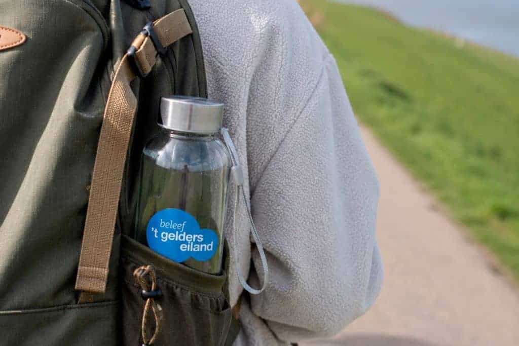 Waterfles met 't Gelders Eiland' logo in rugzak, outdoor omgeving.