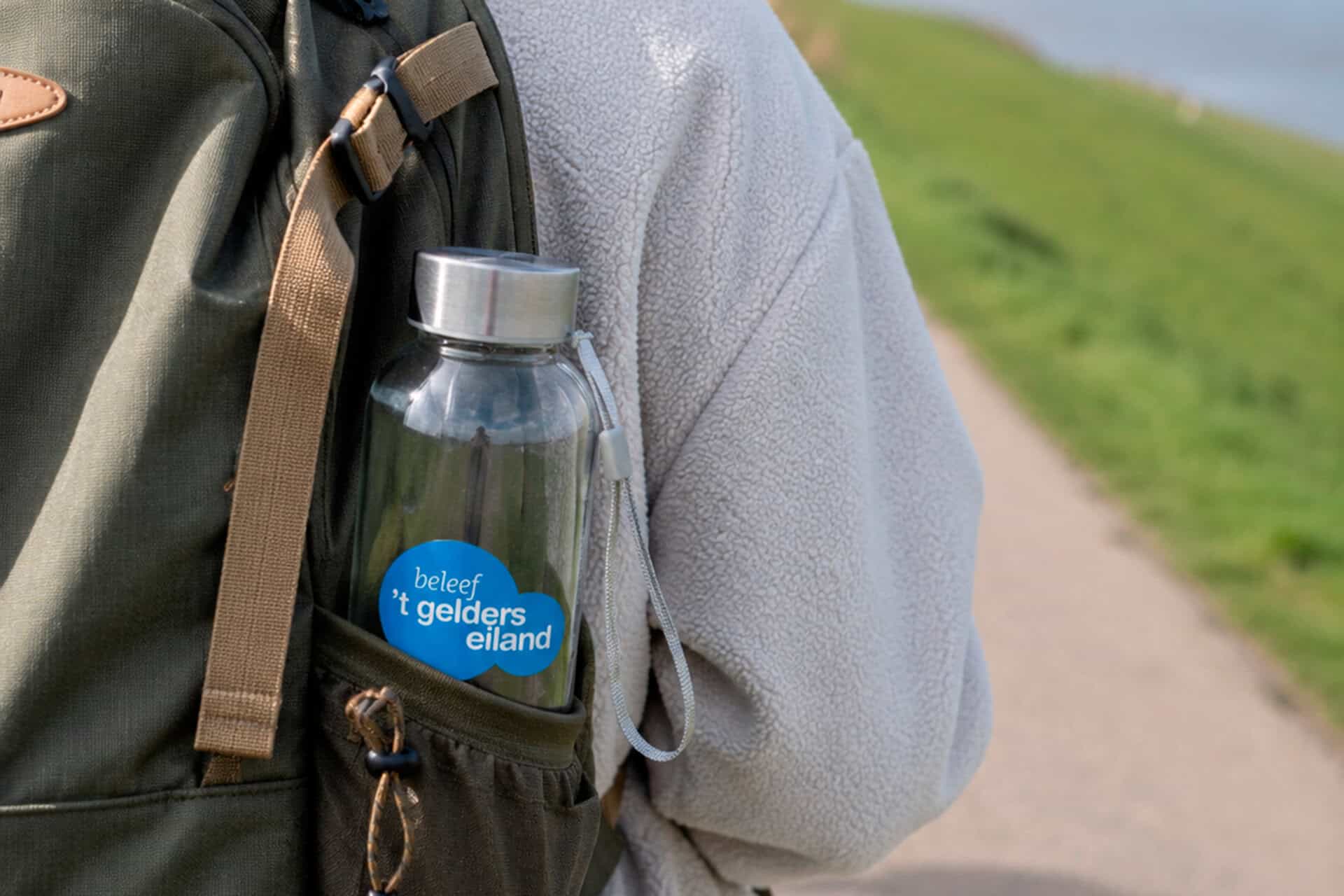 Waterfles met 't Gelders Eiland' logo in rugzak, outdoor omgeving.