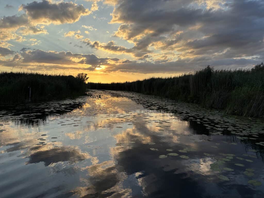 Zonsondergang boven water met wolken en waterlelies op 't Gelders Eiland.