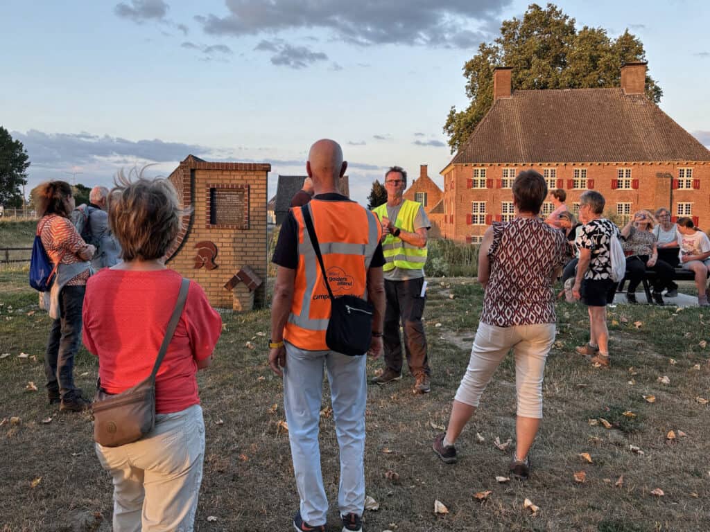 Groep mensen op 't Gelders Eiland tijdens een evenement bij zonsondergang.