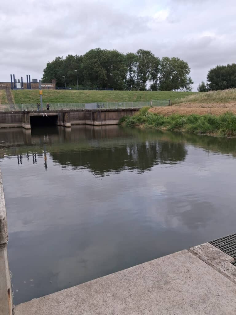 Rustige waterkant met groene bomen en een sluiskade op 't Gelders Eiland.